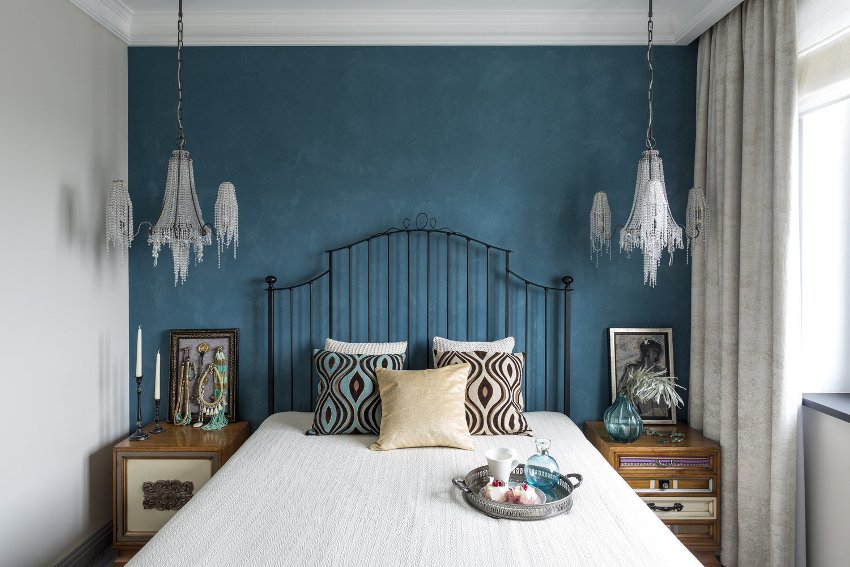 Стена у изголовья кровати, выполненная в акцентной манере с помощью цвета – удачный дизайнерский прием для выделения центрального предмета мебели маленькой спальни